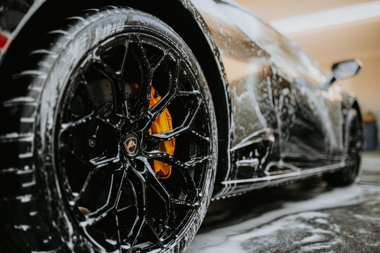Detailed close-up of a luxury car wheel covered in soap suds during a professional car wash.